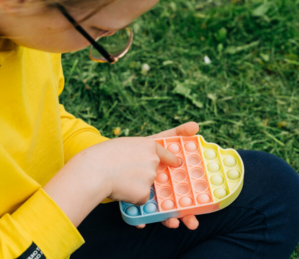 Anonymous child playing with colorful poppit sensory game. Close up of kid hands Push colorful trendy pop bubble flexible fidget toy.